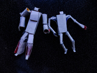 Two handmade cardboard robot figures lying on a dark textured surface, crafted with tape and paper tubes. Creative DIY art concept representing imagination, recycling, and handmade craftsmanship.