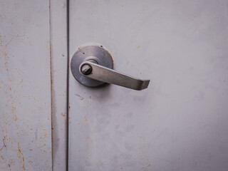 Close-up of a stainless steel lever handle mounted on a metal door with visible scratches and rust stains. Ideal for industrial design, architecture, or maintenance themes.