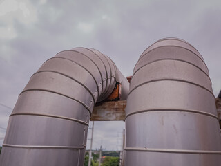 Curved stainless-clad industrial water pipes mounted outdoors with visible joints and supports. Ideal for illustrating infrastructure, HVAC systems, or mechanical design.