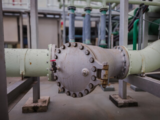 Close-up of a large industrial water pipe with bolted flange and red-handled valve. Clean setup with visible joints and supports in a mechanical facility.