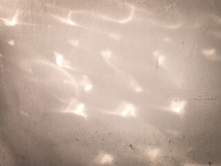 Soft light reflections cast abstract patterns on a textured cement wall. Ideal for backgrounds, design concepts, or artistic compositions with natural ambiance.