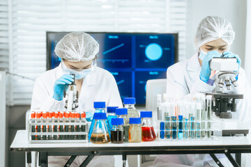 Two focused Asian scientists work in a bright laboratory with microscope, test tubes, and chemical solutions, performing biological, pharmaceutical, and analytical research with scientific precision