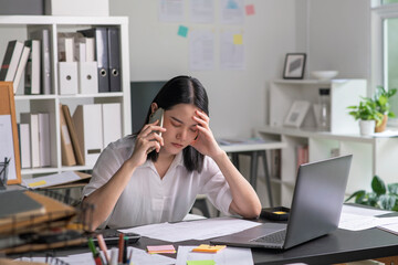 Young Asian Businesswoman looking stressed while talking on the phone, Young businesswoman working at office feels overworked and burnout