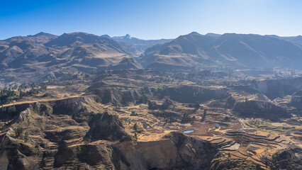 Beautiful mountain landscape. Agricultural terraces, lakes in the valley, and green vegetation are visible on the mountainside. A mountain range against a clear blue sky. Peru. Colca