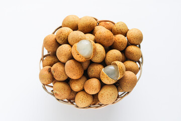 Top view of a pile of longan (kelengkeng) fruits in a woven basket, with two fruit peeled to reveal the translucent white flesh. Isolated on a white background.