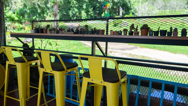 Outdoor Bar: Three yellow bar stools stand at a counter filled with tiny potted succulents with a view of vibrant green nature.