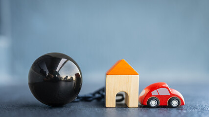 Symbolic image of debt and financial burden, showing a chain ball connected to a house and car....