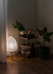 Cozy evening interior of the living room - metal table with decor, lighted paper lamp in Japanese style, ficus on wooden floor