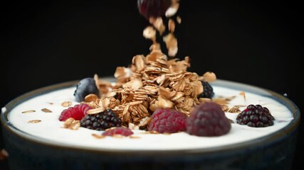 Slow motion close-up of crunchy granola cereal pouring into a healthy breakfast bowl with creamy yogurt, fresh raspberries, blueberries, and blackberries. - Powered by Adobe