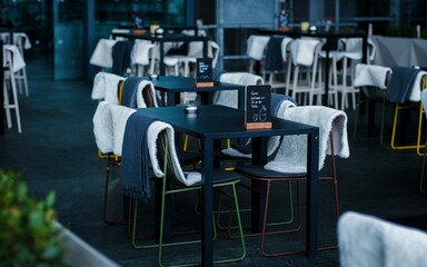 A quiet cafe terrace with black tables and chairs equipped with warm blankets for customer comfort.