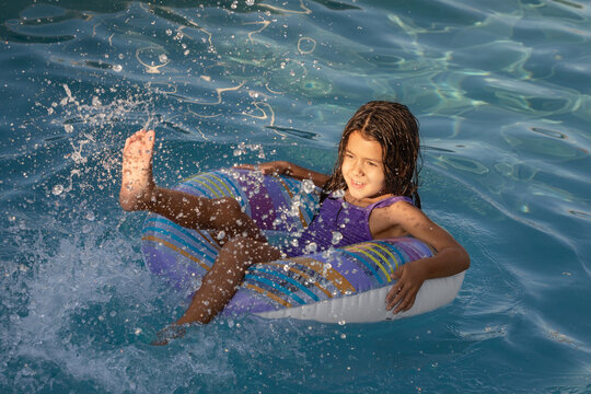 Happy child girl sits on summer pool float and splashes water with her feet