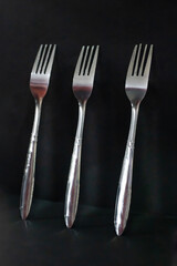 Three Shiny Silver Forks on Dark Black Background
