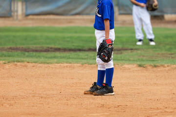 A young boy playing baseball stands on the field. Sports participation for kids aged 6-7.