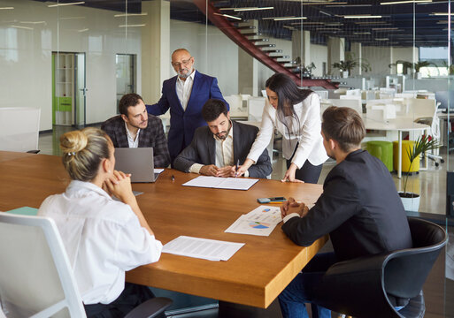 Business meeting for contract signing and discussion by corporate team in modern office. Businesswoman holding pen to sign document and approve agreement with diverse group of colleagues