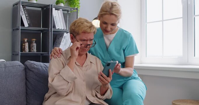 Nurse caregiver supports senior woman using smartphone. She offers homecare guidance, explaining healthcare apps and booking appointments to build confidence. Kind home care help and support.