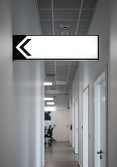 Empty white directional sign with black border in modern office corridor. Modern sign post in professional office hallway with muted lighting.