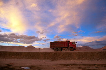 Naklejka premium A red truck driving under the setting sun 
