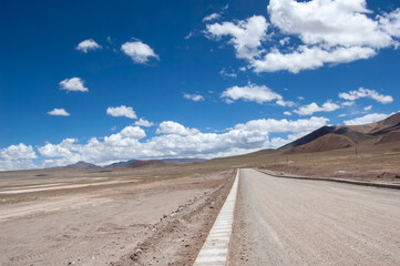 Vast desert road under a clear blue sky with scattered clouds