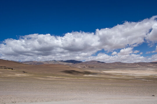 Vast arid plain under a blue sky with scattered clouds
