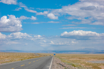 A long road under a blue sky with scattered clouds