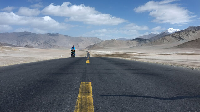 A lone motorcyclist riding on a vast desert road under a clear sky - Powered by Adobe