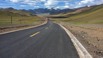 Long straight road in vast open mountainous area under blue sky