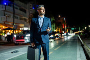 Obraz premium Businessman chatting on phone in night street. Businessman using smartphone. Ambitious businessman chatting online. Businessman walking night city. Business man chat on cellphone outdoor