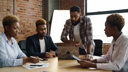 Four diverse african american business professionals, two men two women, collaborate around a modern table, red brick walls, laptop, tablet, soft light, shallow depth. Productive teamwork concept - Powered by Adobe
