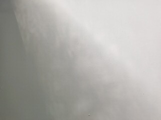 A soft gradient of light and shadow creates a gentle ambiance on a plain wall. The surface exhibits a muted texture that enhances the reflective quality.