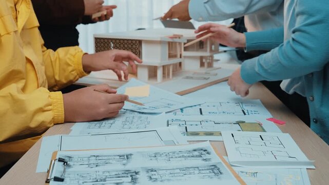 A group of professionals actively collaborating on architectural designs, focusing on blueprints and models within a creative workspace environment, showcasing teamwork. SACTR