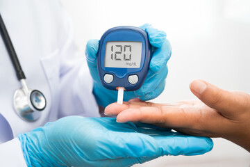 Asian doctor using digital glucose meter for check sample blood sugar level to treatment diabetes.