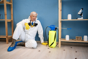 Disinfection worker from pest control service in protective suit and respirator mask sitting on...
