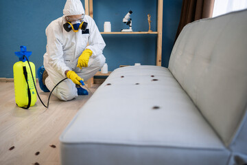 Pest control exterminator in protective suit and respirator mask with yellow sprayer spraying...