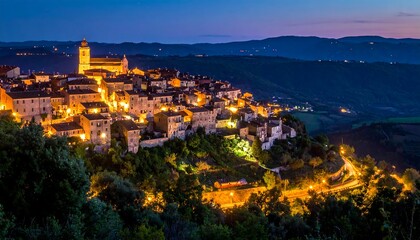 Obraz premium A beautiful nighttime vista captures an ancient Italian hilltop town. Warm golden lights illuminate buildings, church tower, and winding roads