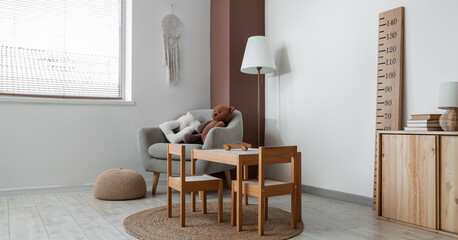 Armchair, table, chairs, stadiometer and floor lamp in interior of light children's room