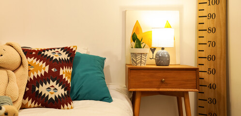 Comfortable bed, table, stadiometer and glowing lamp in interior of children's room