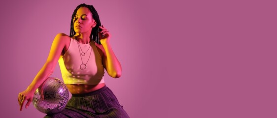 Beautiful young African-American woman holding disco ball on color background with space for text