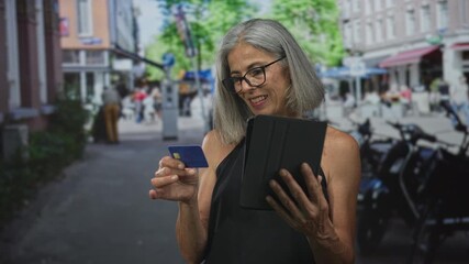 Woman holding tablet and creditcard on street, bare shoulders and hands visible while tapping screen with smile; confidence. - Powered by Adobe