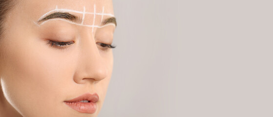 Beautiful young woman with marking for eyebrows correction against grey background, closeup
