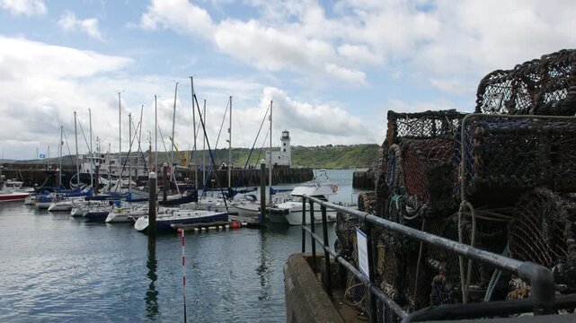 Fishing nets and ropes stacked on the harbor edge in Scarborough, North Yorkshire in England, with boats docked nearby and a lighthouse across the calm water