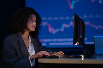 Professional businesswoman or financial analyst working late, focusing on stock market data