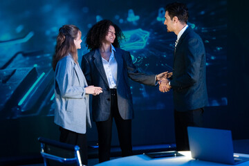 Diverse cybersecurity team celebrating a successful project with hugs and handshakes in a modern office.