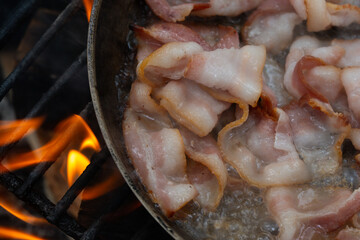 Sizzling bacon in a pan on an open fire cooking outdoors