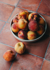 Close up of bowl of peaches on terra cotta tile background.