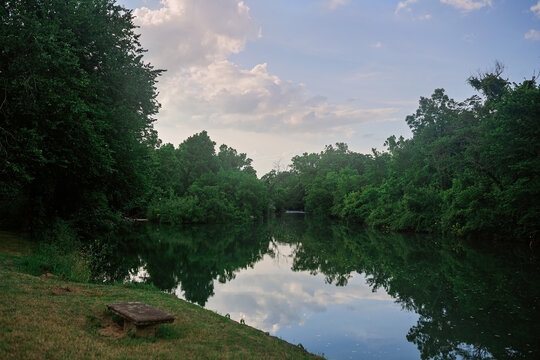 Still river reflecting trees and sky with grassy bank and bench