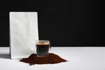 Bag with coffee powder and glass of hot espresso on white table