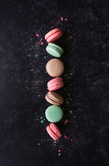Top view line of assorted macaron cookies on black background.