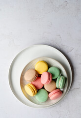 Top view of plate of assorted colorful macarons on white background.