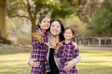 Fototapeta premium Mom hugs daughters while smiling with fall leaves