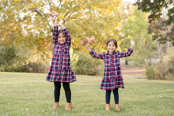 Fototapeta premium Sisters cheerfully raise fall leaves in the park
